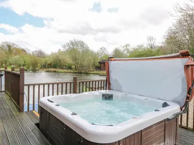 a hot tub on a deck next to a river at Woodpecker Lodge in Langham
