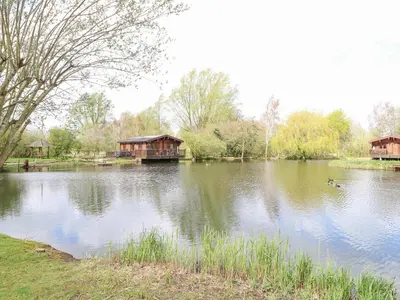 a lake with a house and ducks in the water at Woodpecker Lodge in Langham