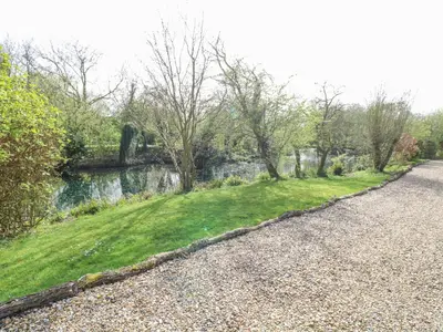 a gravel road next to a river with trees at Kingfisher Lodge in Langham