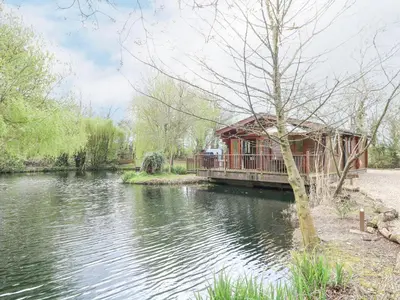 a house on a dock next to a body of water at Kingfisher Lodge in Langham