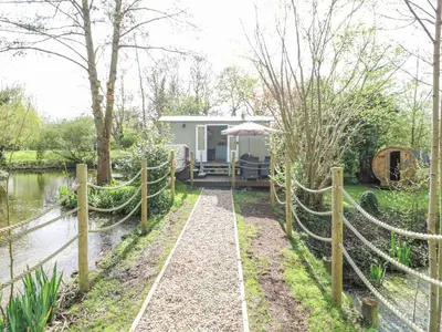 a cottage in the middle of a river with a fence at Damsel Shepherds Hut in Badwell Ash