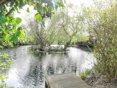 a river with a wooden boardwalk and trees on it at Heron Lodge in Langham