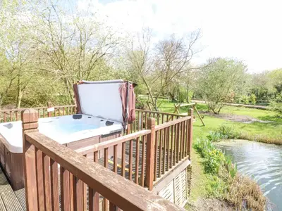 a hot tub sitting on a deck next to a river at Wagtail Lodge in Langham