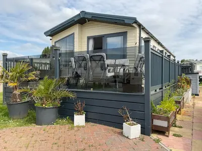 a house with a deck with chairs and plants at 2 bedroom Mini Lodge Caravan at Coopers Beach Holiday Park in East Mersea