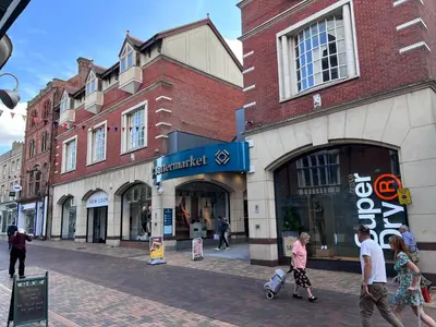 a group of people walking down a street in front of a store at St Nicolas Cottage in Ipswich