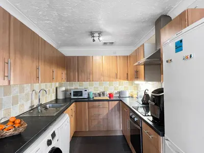 a kitchen with wooden cabinets and a white refrigerator at Casa di Qeis a double bedroom ground floor flat with free parking in Chesterton