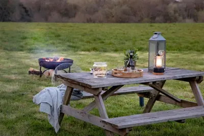a picnic table with a lantern and a fire in a field at Cuckoo - Sweffling Hall in Rendham