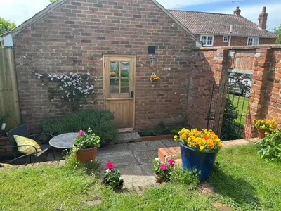 a garden with a brick house with a table and flowers at The studio spring house in Alderton