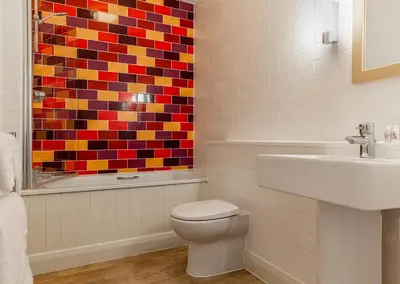 a bathroom with a toilet and a colorful mosaic on the wall at The Brudenell in Aldeburgh