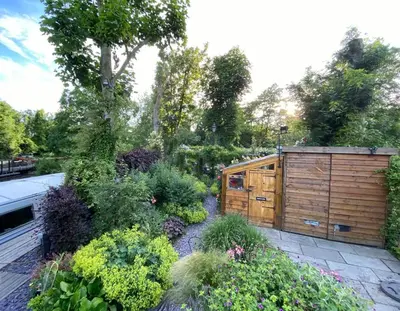 a garden with a wooden building and some plants at River Mill Retreat in Little Hallingbury