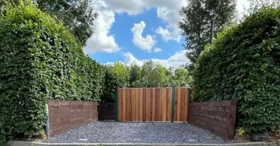 a fence with a wooden gate in between two bushes at River Mill Retreat in Little Hallingbury