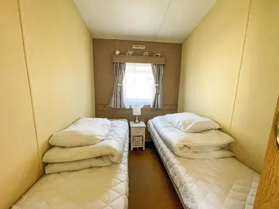 two beds in a small room with a window at Caravan With Large Decking At Coopers Beach Holiday Park Ref 49036Ts in East Mersea