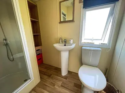 a bathroom with a toilet and a sink and a window at Caravan With Large Decking At Coopers Beach Holiday Park Ref 49036Ts in East Mersea