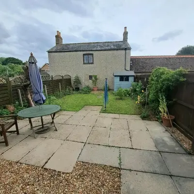 a patio with a table and an umbrella and a house at Cute little 2 bed near Cambridge in Fenstanton