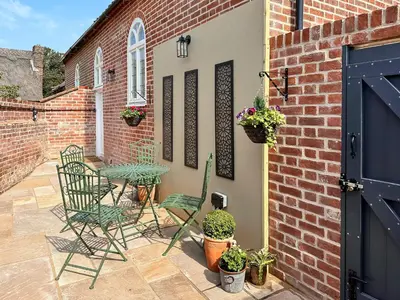 a patio with a table and chairs and a brick wall at The Church Rooms in Wenhaston