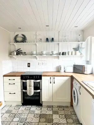 a kitchen with white cabinets and a black stove at Cosy Cottage in Mersea - Walking distance to beach and town in West Mersea