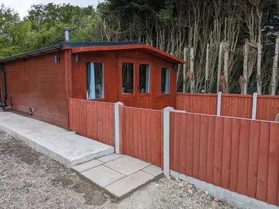 a small wooden house next to a fence at Meadow Lodge in Billericay