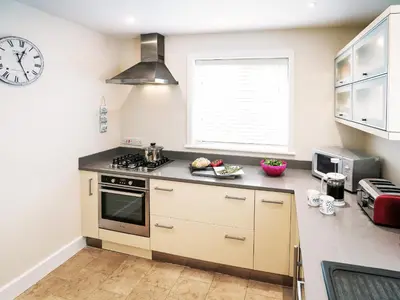 a kitchen with a stove and a clock on the wall at Cannon Corner by The Suffolk Cottage Collection in Aldeburgh