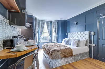 a bedroom with blue walls and a bed and a kitchen at Studio Apartments in Southend in Southend-on-Sea