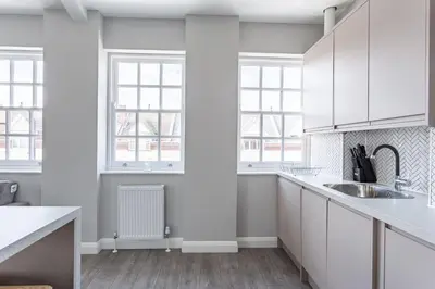 a white kitchen with white cabinets and windows at St Johns Apartments & Studios Southend in Southend-on-Sea