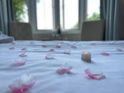 a candle sitting on top of a bed with pink rose petals at Beaches Guest House in Southend-on-Sea