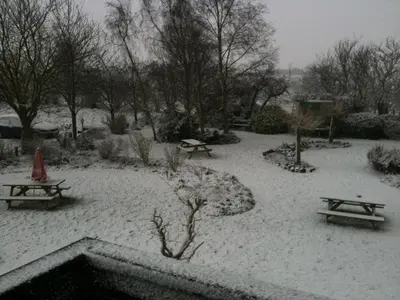 a garden covered in snow with picnic tables and benches at Six Bells Inn in Bardwell
