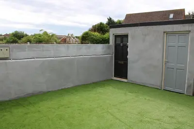 a backyard with a concrete wall and green grass at 12 Penn Gardens - Apart 1 in Friern Barnet