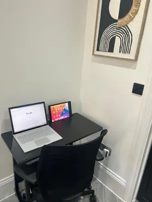 a laptop computer sitting on a black desk with a chair at Stylish Flat in London in Harold Wood