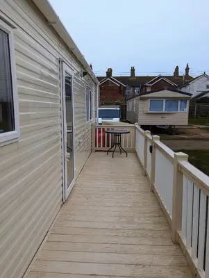 a wooden walkway with a table on the side of a house at Van-Tastic 6 berth static in Felixstowe