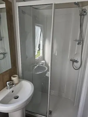 a white bathroom with a shower and a sink at Highfield Grange Holiday Park in Clacton-on-Sea