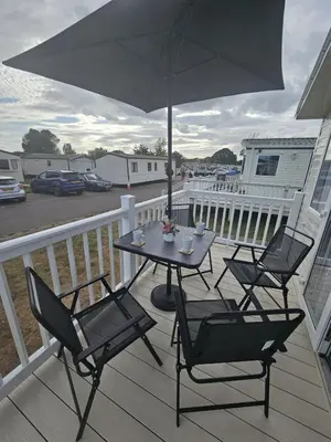 a table and chairs on a deck with an umbrella at Highfield Grange Holiday Park in Clacton-on-Sea