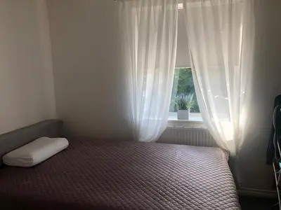 a bedroom with a bed and a window with white curtains at Basildon, private room in a flat in Basildon