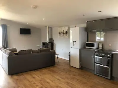 a living room with a couch and a kitchen at Nightingale Lodge - Adults Only in Lackford