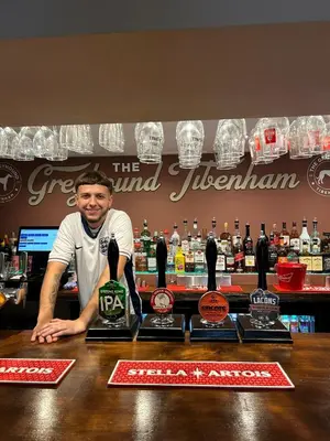 a man standing behind a bar with three awards at The Greyhound Pub in Tibenham