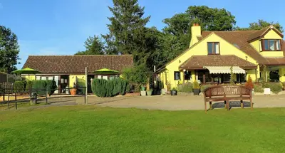 a yellow house with a bench in the grass at Annexe at Gosfield Lake in Gosfield