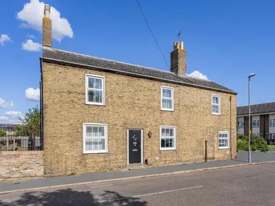 a brick building with two chimneys on a street at Cathedral View Farmhouse in Ely