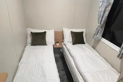 two twin beds in a small room with a window at 3 Bedroom Caravan - Sleeps 8 - Parking Wifi Pool in Clacton-on-Sea