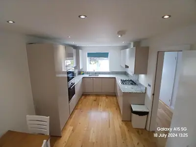 a kitchen with white cabinets and a wooden floor at Hornchurch House - Jackson Close in Harold Wood