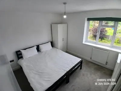 a bedroom with a bed with white sheets and a window at Hornchurch House - Jackson Close in Harold Wood