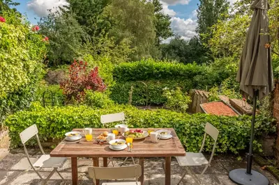 a wooden table in a garden with an umbrella at Brimming with Medieval charm - Weavers Cottage in Lavenham