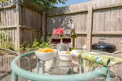 a glass table with two glasses of wine and snacks at Olive Cottage, Wickham Market in Wickham Market