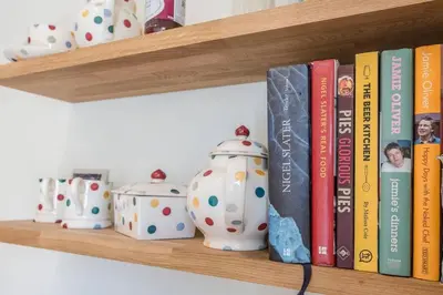 a wooden shelf with books and vases and books at Olive Cottage, Wickham Market in Wickham Market