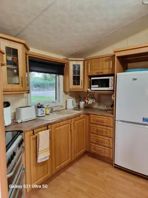 a kitchen with wooden cabinets and a white refrigerator at The Duck - Free Fishing, pets welcome - static caravan in Clare, Suffolk in Sudbury