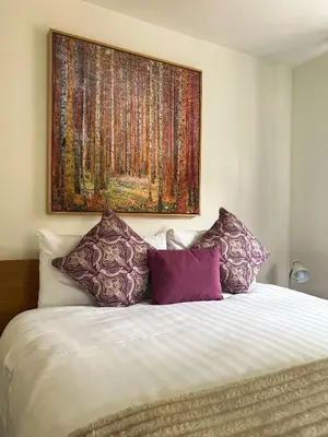 a large painting above a bed with purple pillows at Westminster College Cottages, Cambridge in Cambridge