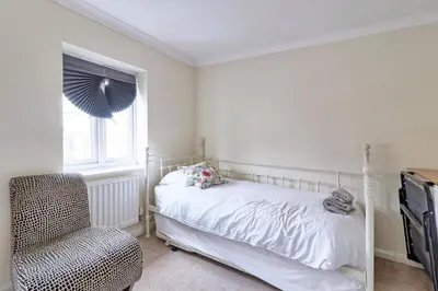 a bedroom with a bed and a chair and a window at By Buildersbeds - Paignton House 4 Bedrooms in Harold Wood