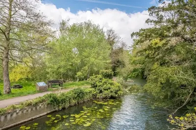 a river in a park with a bench and trees at The Old Woodstore in Sudbury