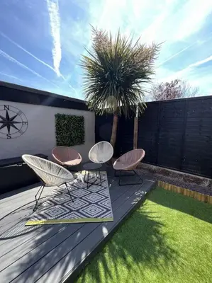 a deck with two chairs and a table and a palm tree at By Buildersbeds - Heaton House 2 Bedrooms in Havering atte Bower