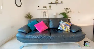 a black leather couch with colorful pillows on it at Apartment at Addenbrooke hospital and Bio Campus - Free Private parking in Cambridge