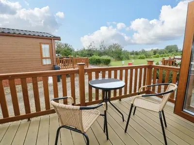a patio with two chairs and a table on a deck at Lodge 26, Fishing Lakes in Stowmarket