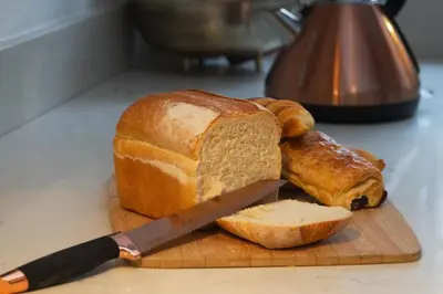 a cutting board with a loaf of bread and a knife at Luxury 2 Bed Manor House Hot Tub Cinema Room SkyTV in Saffron Walden
